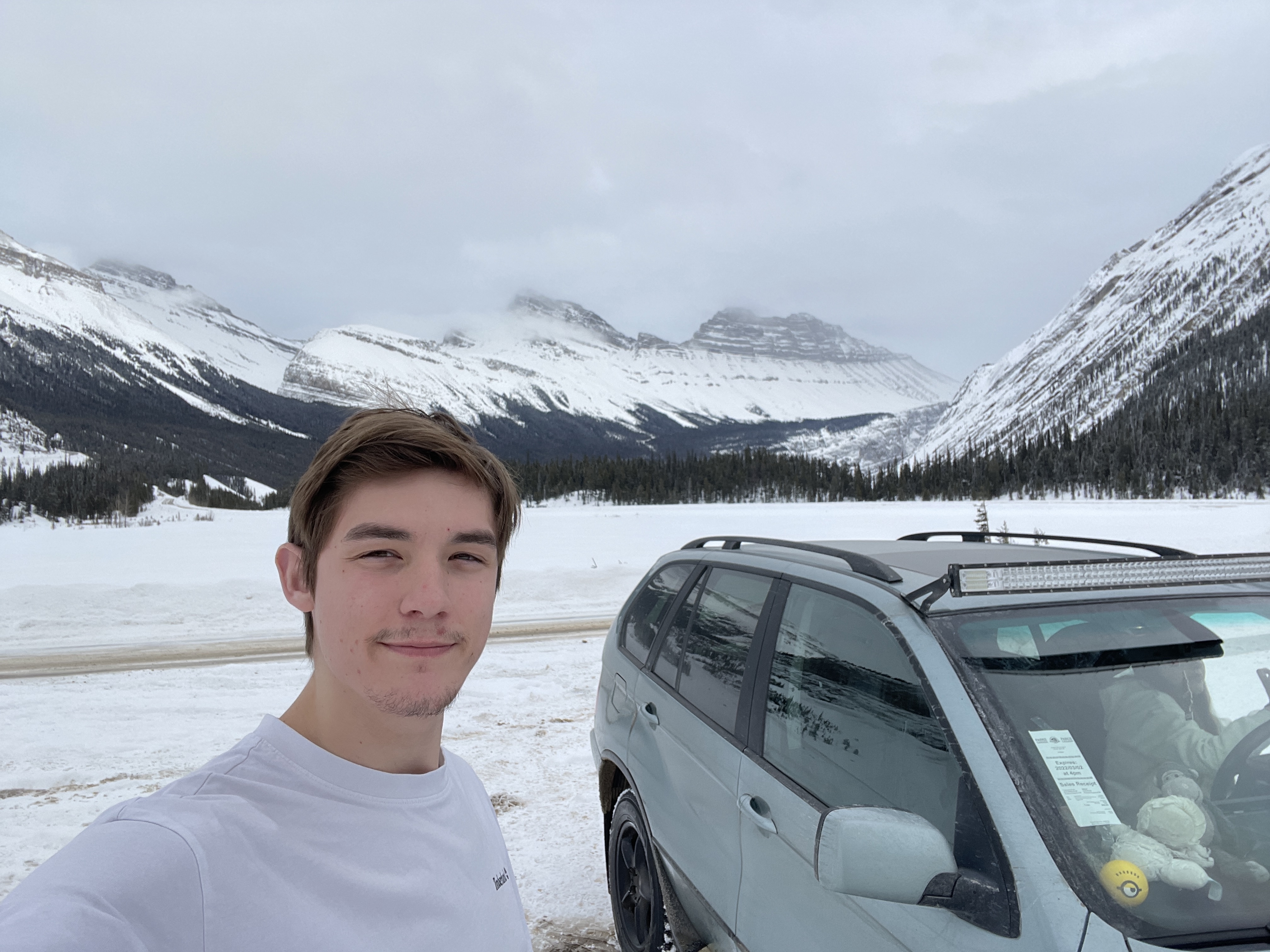 Ryan, standing in the rockies taking a selfie with a car in the background